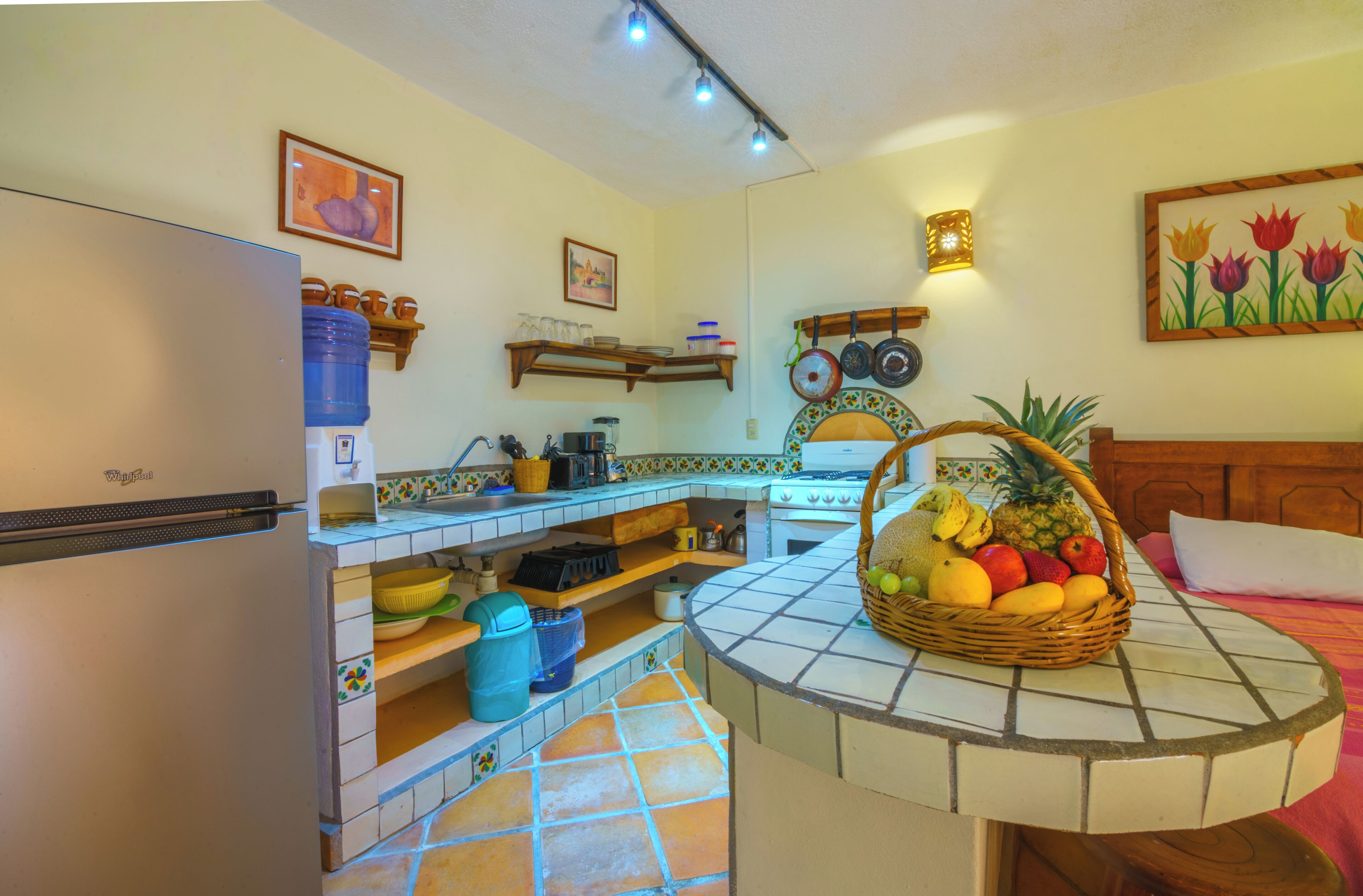A kitchen with a refrigerator, stove, and a fruit basket on the counter.
