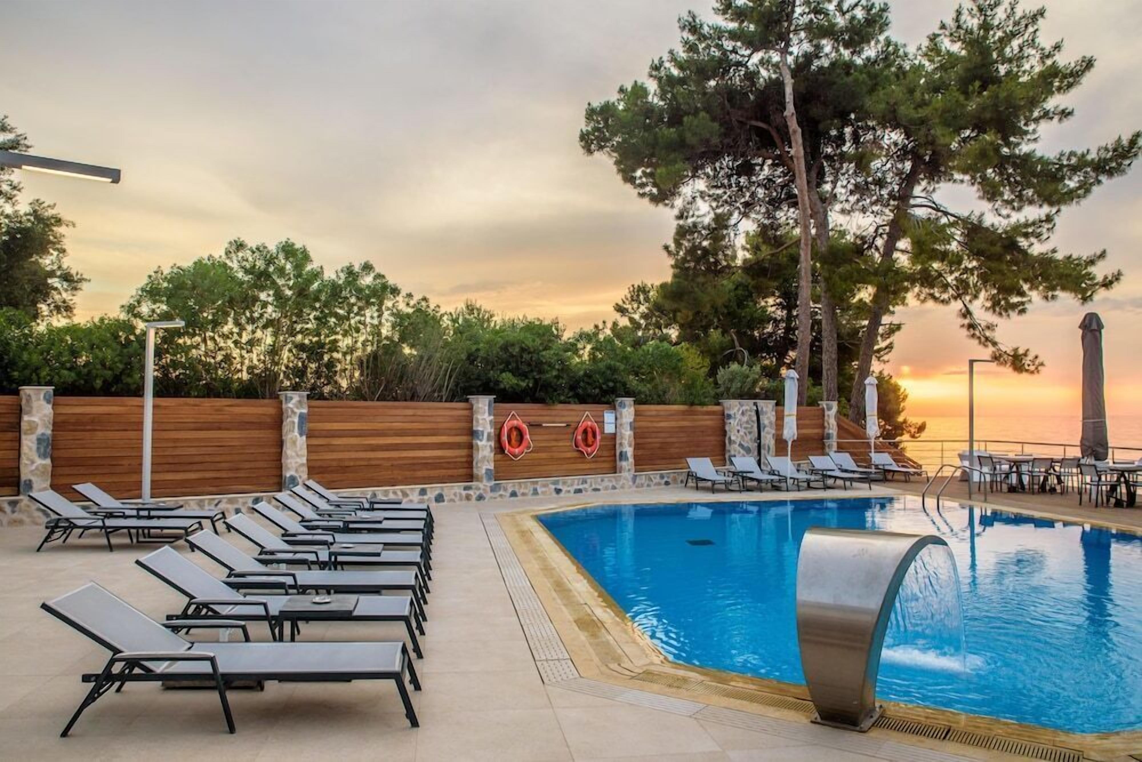 A swimming pool with lounge chairs, a wooden fence, and trees in the background.