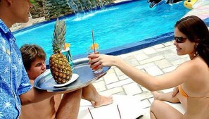 Escena junto a la piscina con una persona sosteniendo una bandeja con una piña y una bebida.