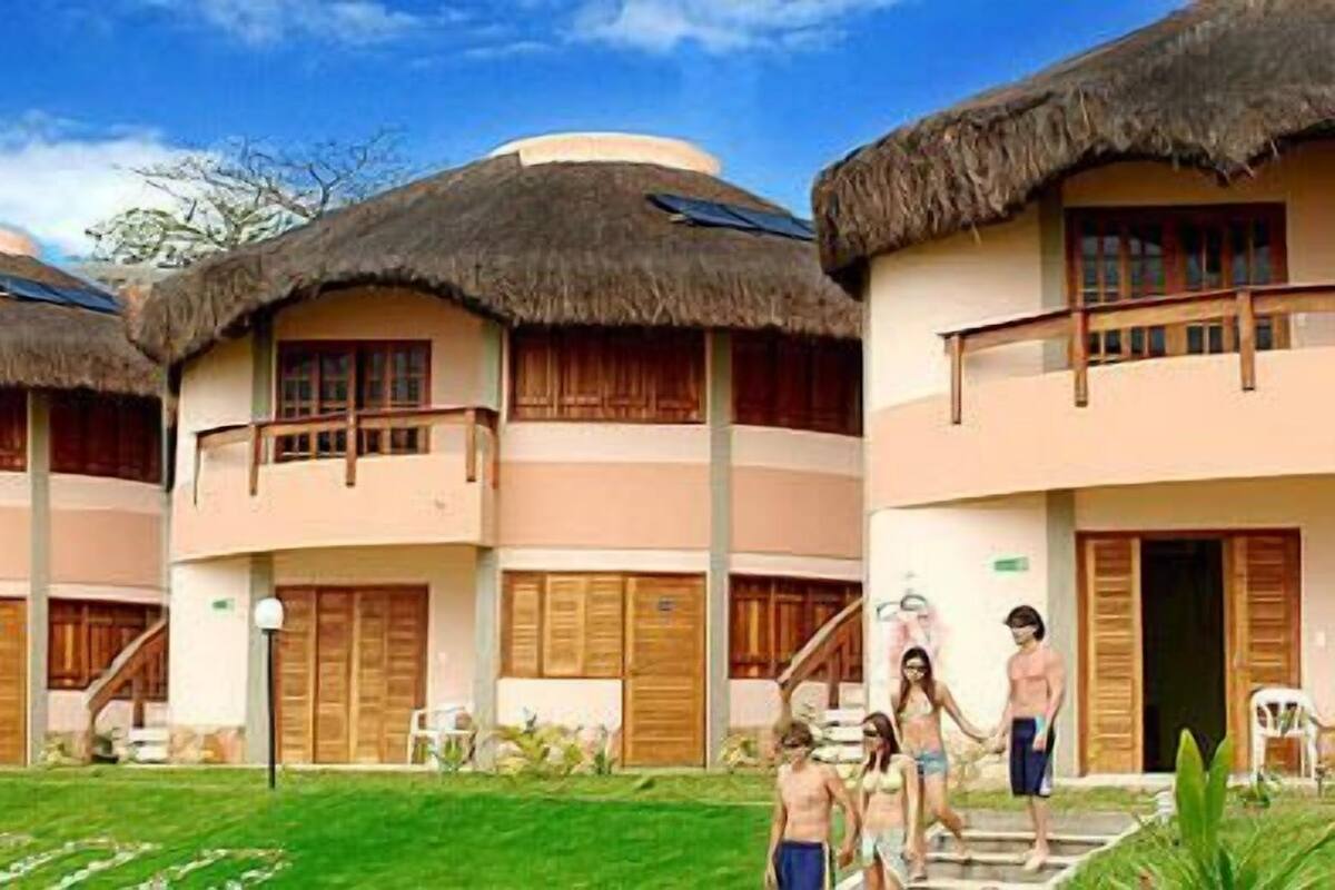 Un resort con edificios de techo de paja, una escalera central y un césped bien cuidado.