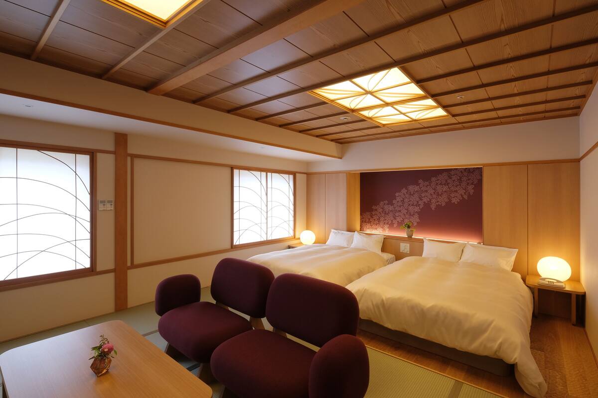 A traditional Japanese-style room with tatami flooring, two beds, a wooden ceiling, and a large window with a decorative screen.
