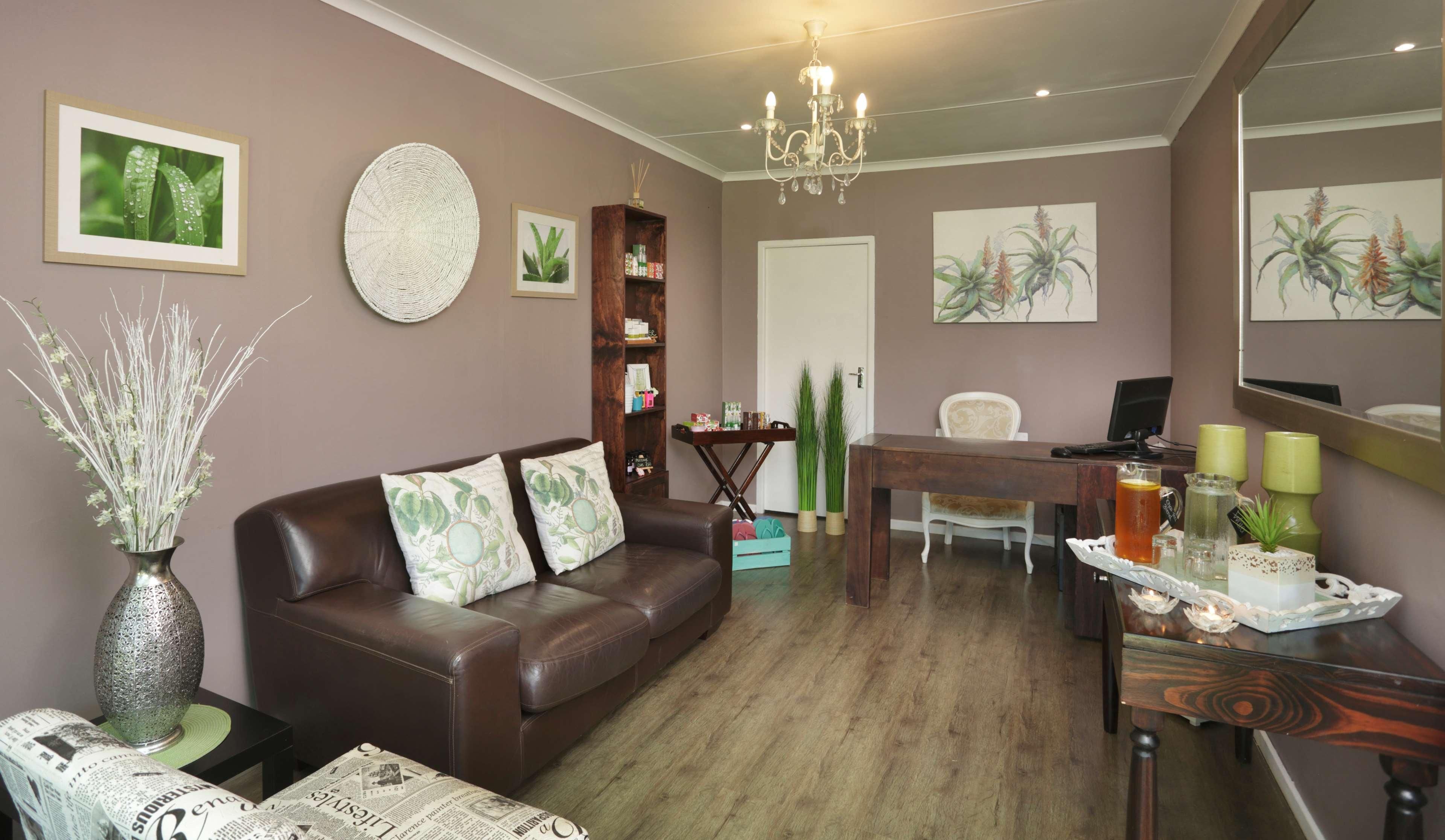 A living room with a brown leather sofa, a coffee table with newspapers, a bookshelf, a dining table with a chair, and a chandelier.