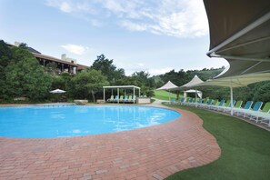 A swimming pool with a brick pathway, lounge chairs, and a gazebo. - Drakensberg Sun (Cathkin Park)