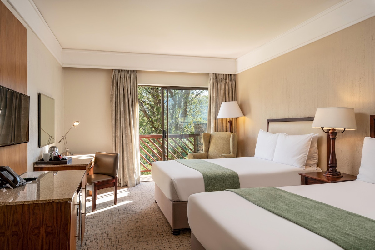 A hotel room with two beds, a desk, a chair, a TV, and a window with curtains.