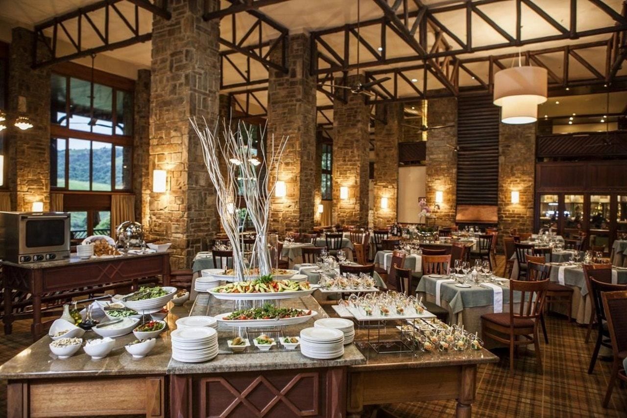 Un comedor amplio con varias mesas dispuestas para una comida, paredes de piedra y un techo alto con vigas a la vista.