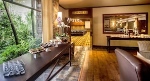 A hotel lobby with a wooden reception desk, a seating area, a large mirror, and a view of the outdoors. - Drakensberg Sun (Cathkin Park)