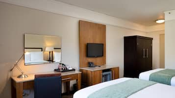 A hotel room with a desk, chair, two beds, a television, and a wardrobe.