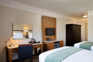 Une chambre d’hôtel équipée d’un bureau, d’une chaise, de deux lits, d’une télévision et d’une armoire.
