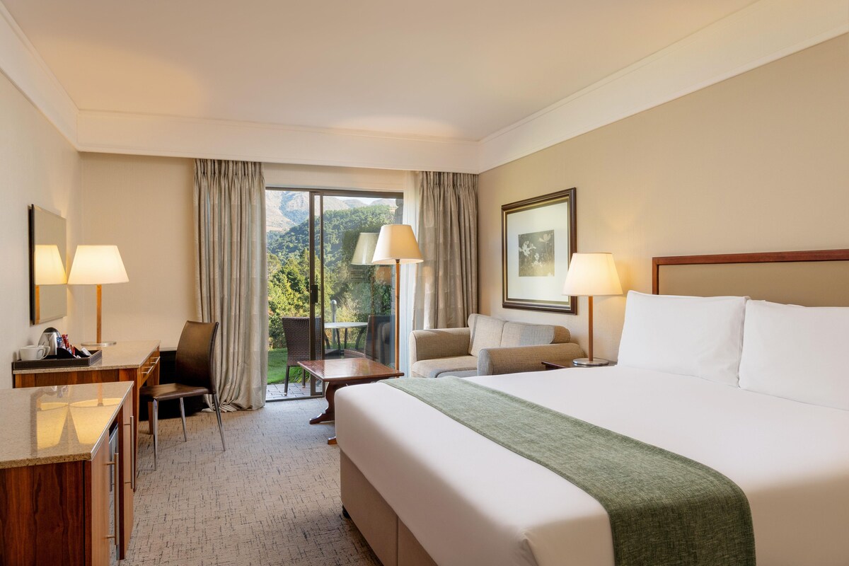 A hotel room with a bed, two chairs, a desk, and a view of the outdoors.