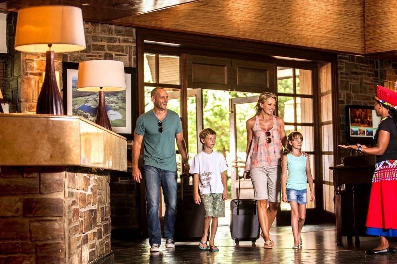 A family walking through a lobby with a stone wall, a wooden ceiling, and a large window.