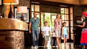 A family walking through a lobby with stone walls, large windows, and a wooden ceiling. - Drakensberg Sun (Cathkin Park)