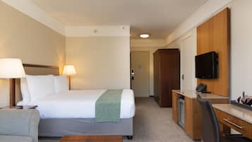 A hotel room with a bed, bedside lamps, a desk with a chair, a television, and a wardrobe.