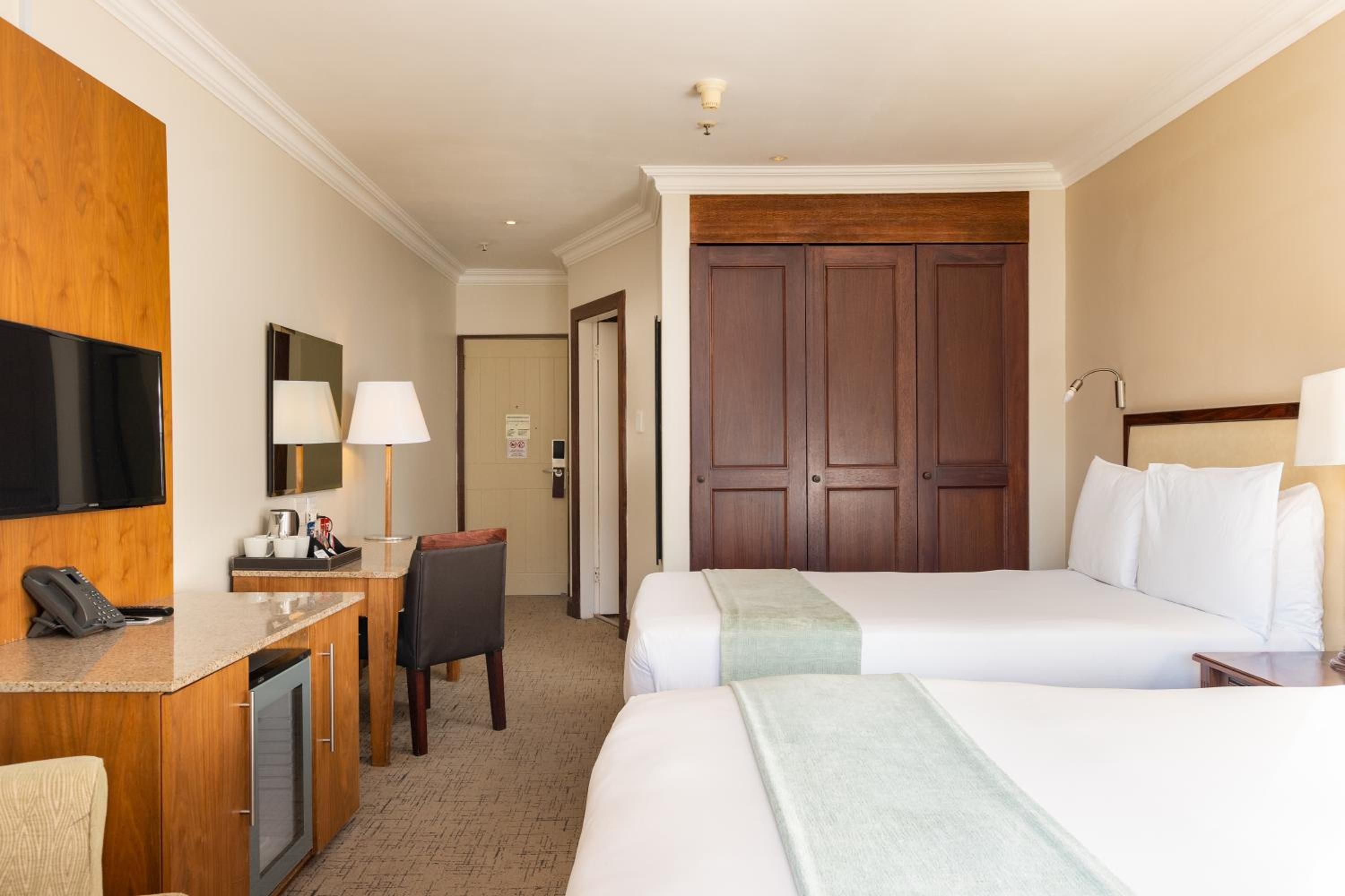 A hotel room with a bed, bedside table, lamp, desk with phone, chair, and a TV mounted on the wall.
