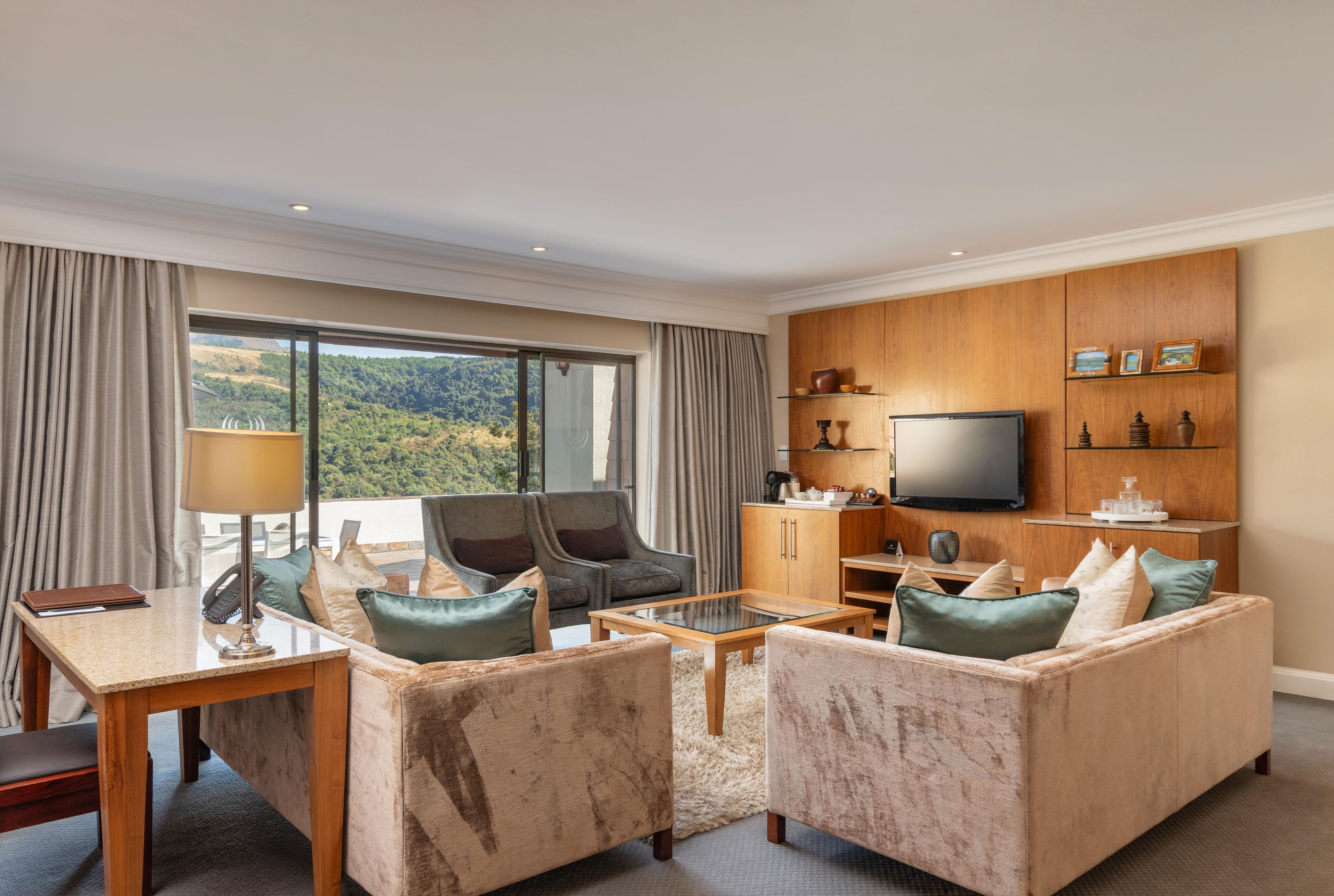 Een hotelkamer met een zithoek, een salontafel, een televisie en uitzicht op het omliggende landschap.