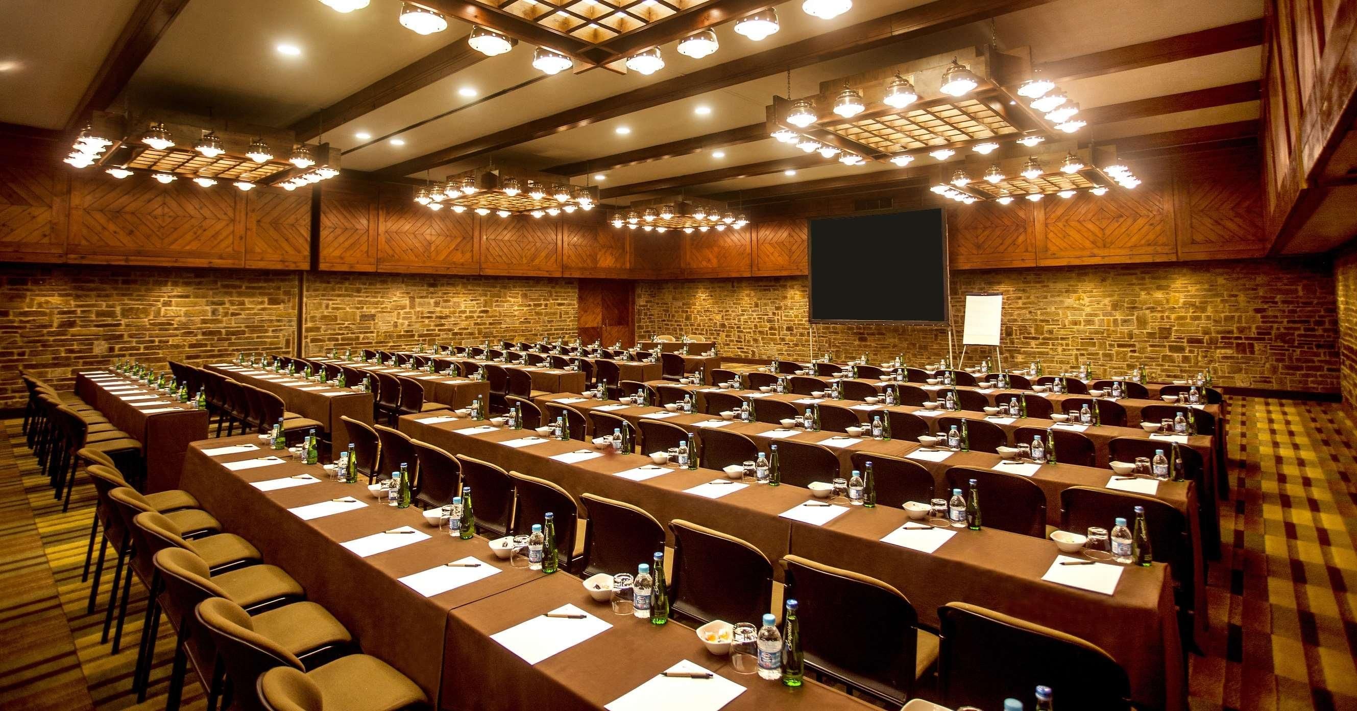 A conference room with multiple tables, chairs, and a large screen.