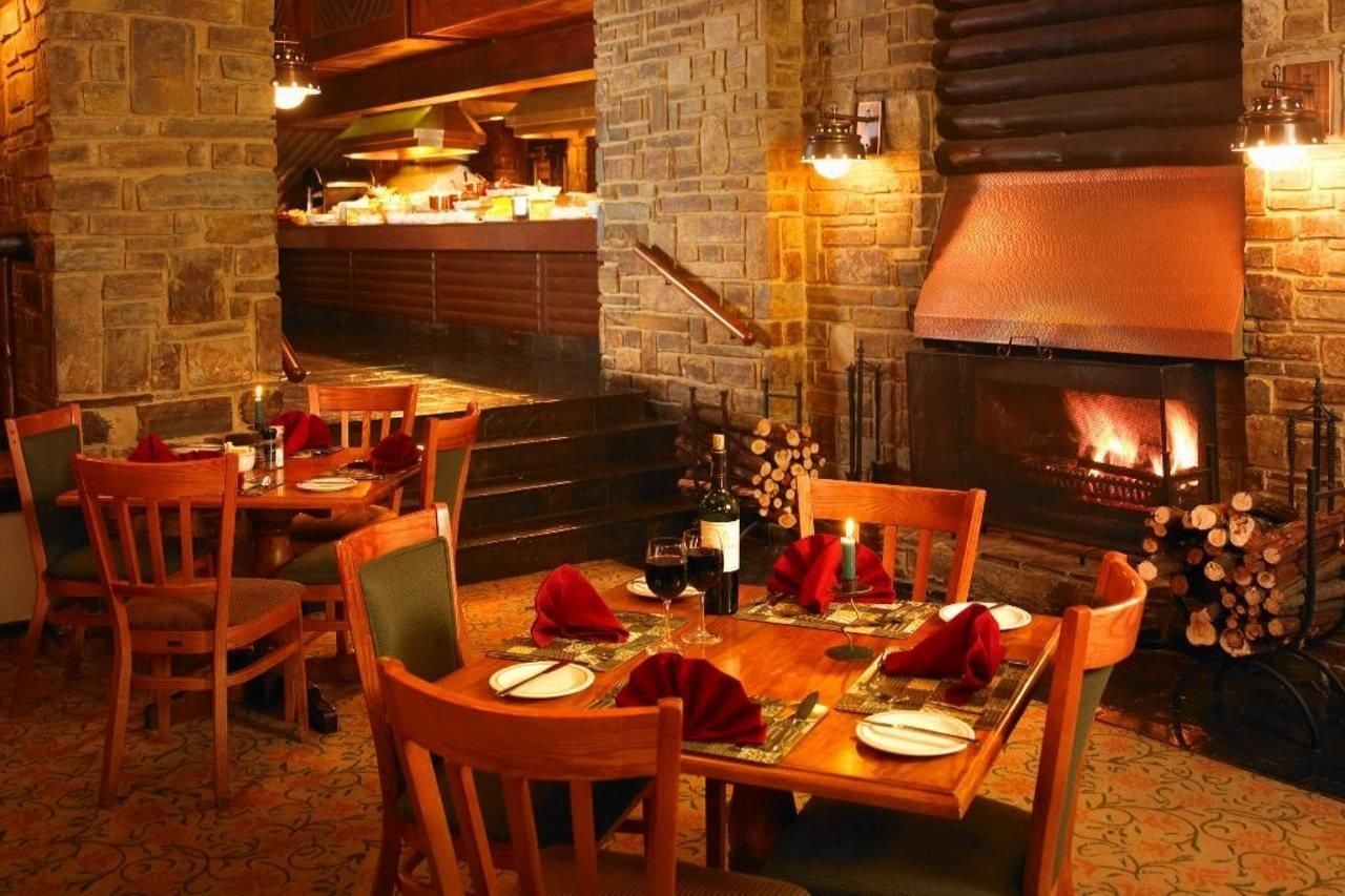 Un restaurant chaleureux avec une cheminée en pierre, des tables en bois et des chaises disposées pour le repas.