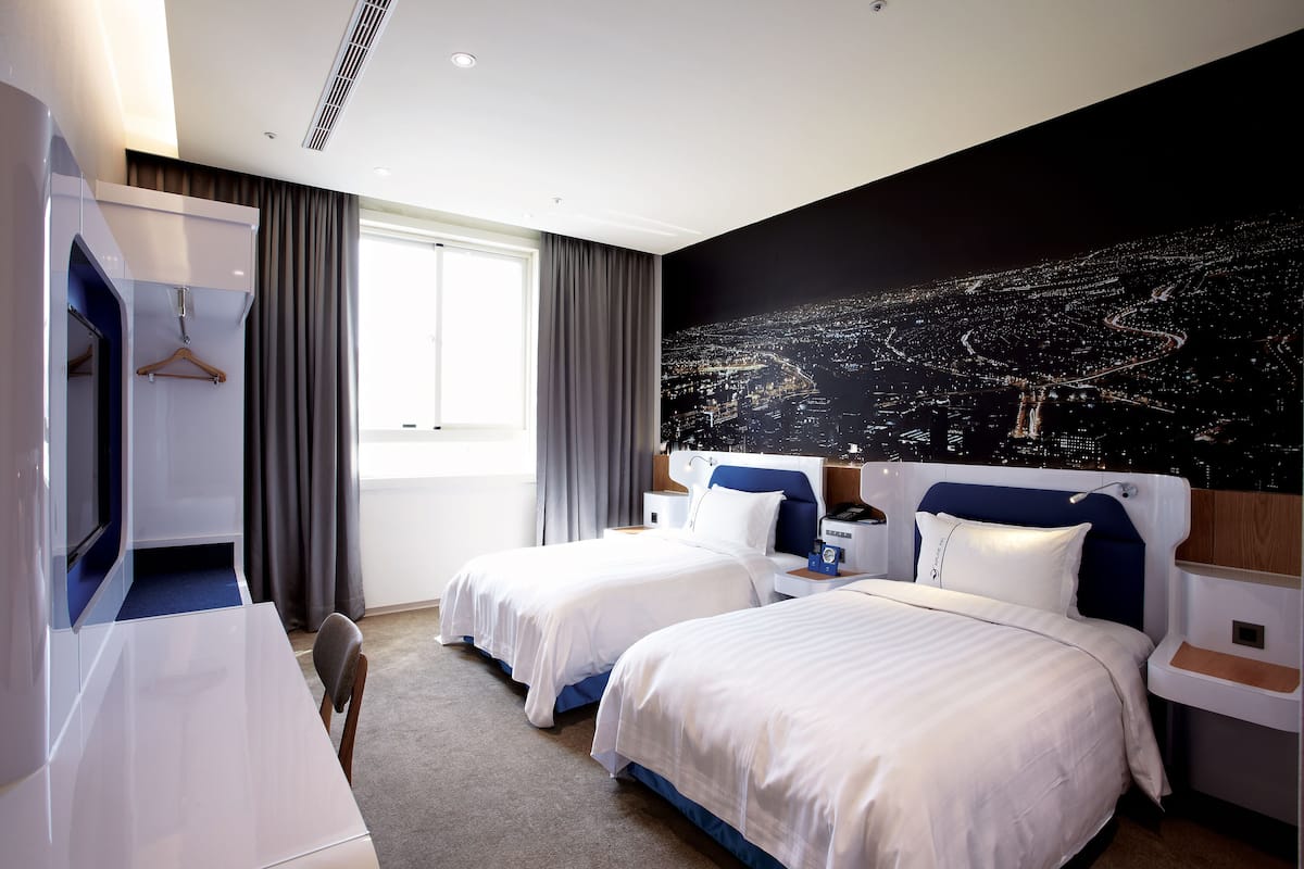 Une chambre d’hôtel avec deux lits, un bureau, une armoire et une vue sur la ville.