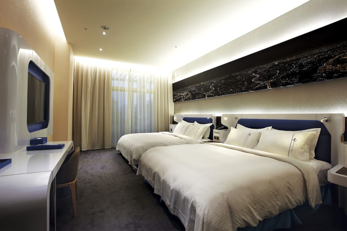 Une chambre d’hôtel avec deux lits, un bureau et une grande fenêtre avec des rideaux.