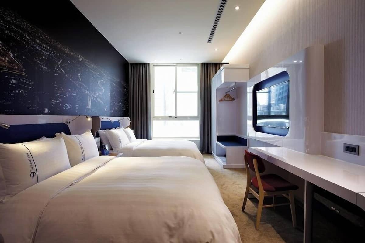 Une chambre d’hôtel avec deux lits, un bureau, une chaise, une télévision et un mur décoré d’une vue sur la ville.