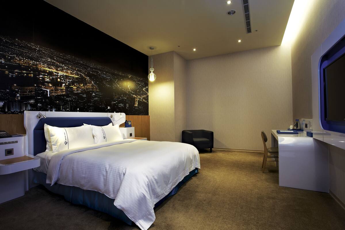 Une chambre d’hôtel moderne avec un grand lit, un bureau et une fresque représentant un paysage urbain sur le mur.