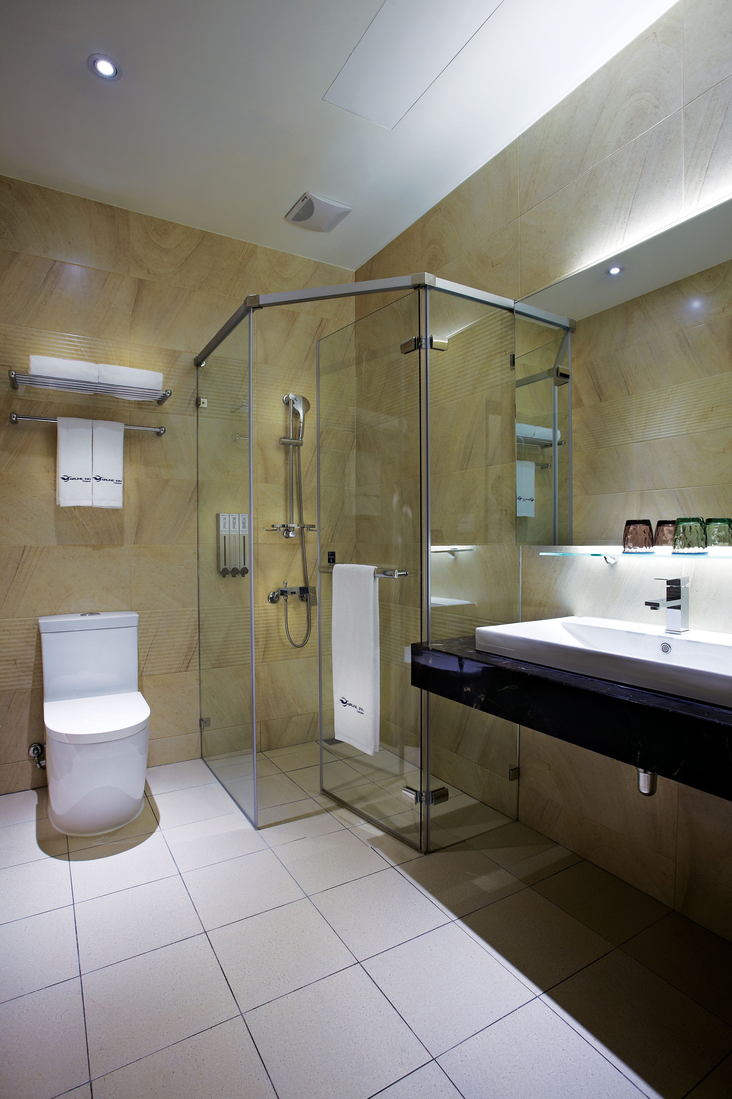 Une salle de bain moderne avec une douche à parois de verre, des toilettes blanches et un grand miroir au-dessus du lavabo.