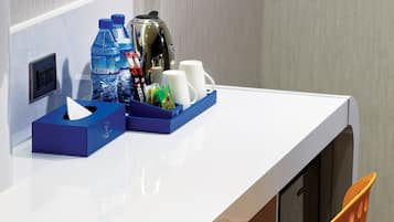 A white desk with a blue tissue box, two water bottles, a thermos, and a mug. An orange chair is partially visible.