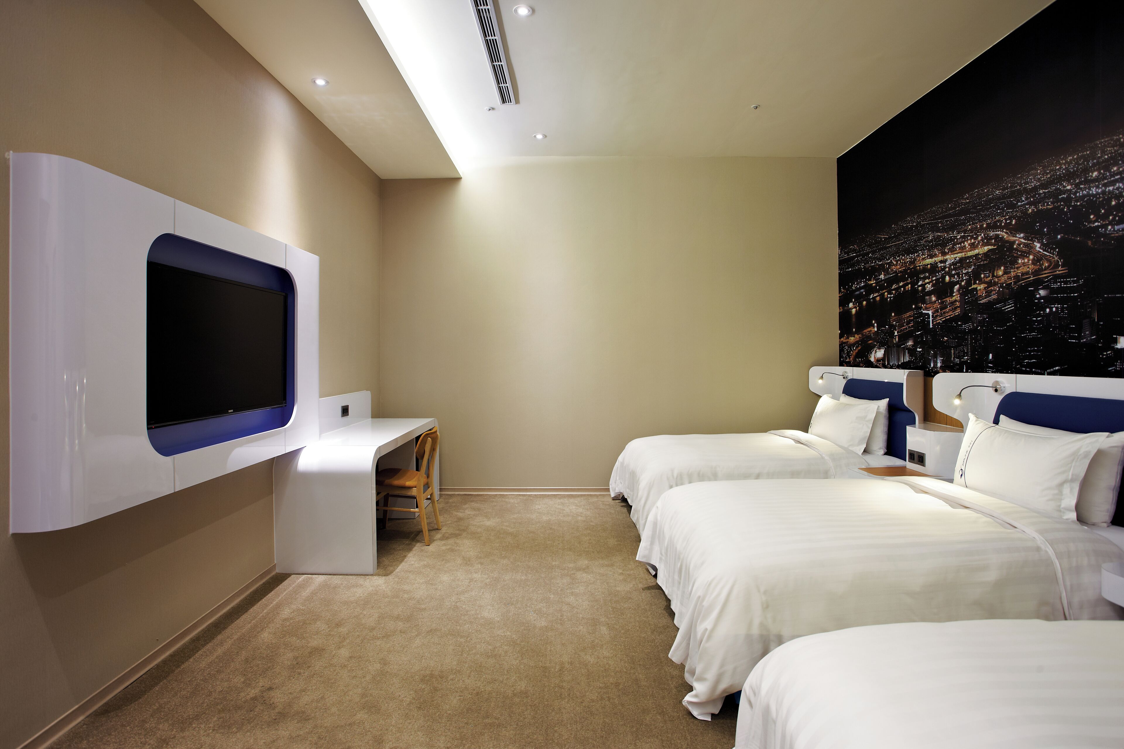 A hotel room with two beds, a desk, and a large TV mounted on the wall.