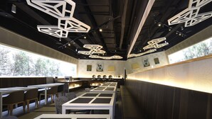 Ein modernes Restaurant mit einer langen Theke, verschiedenen Sitzbereichen und besonderen geometrischen Pendelleuchten.