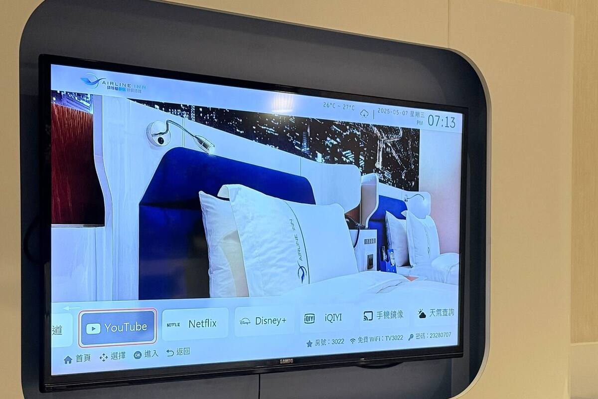 Un écran de télévision affichant une chambre d’hôtel avec un lit, des oreillers et une table de chevet.