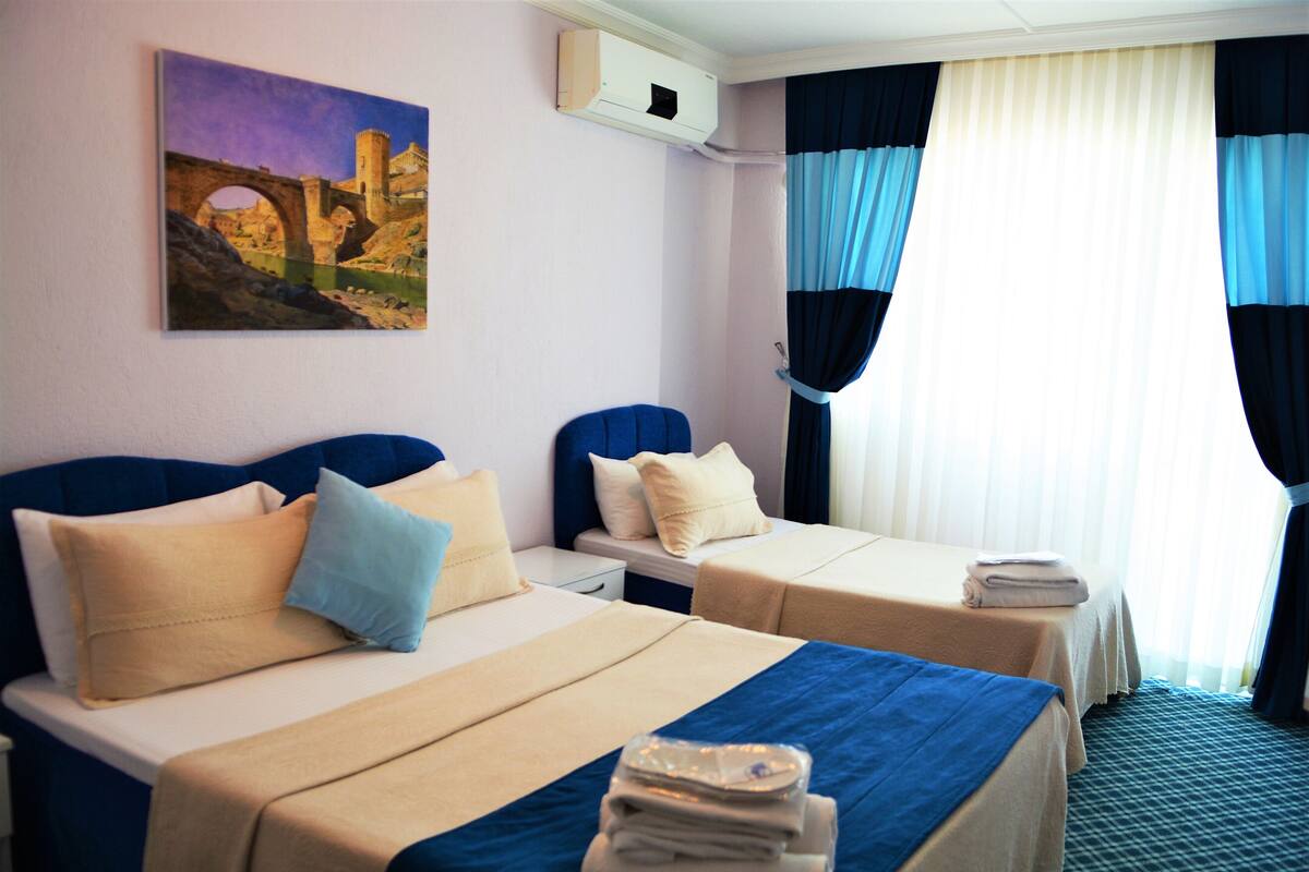Une chambre d’hôtel avec deux lits, un tableau au mur et une fenêtre avec des rideaux.