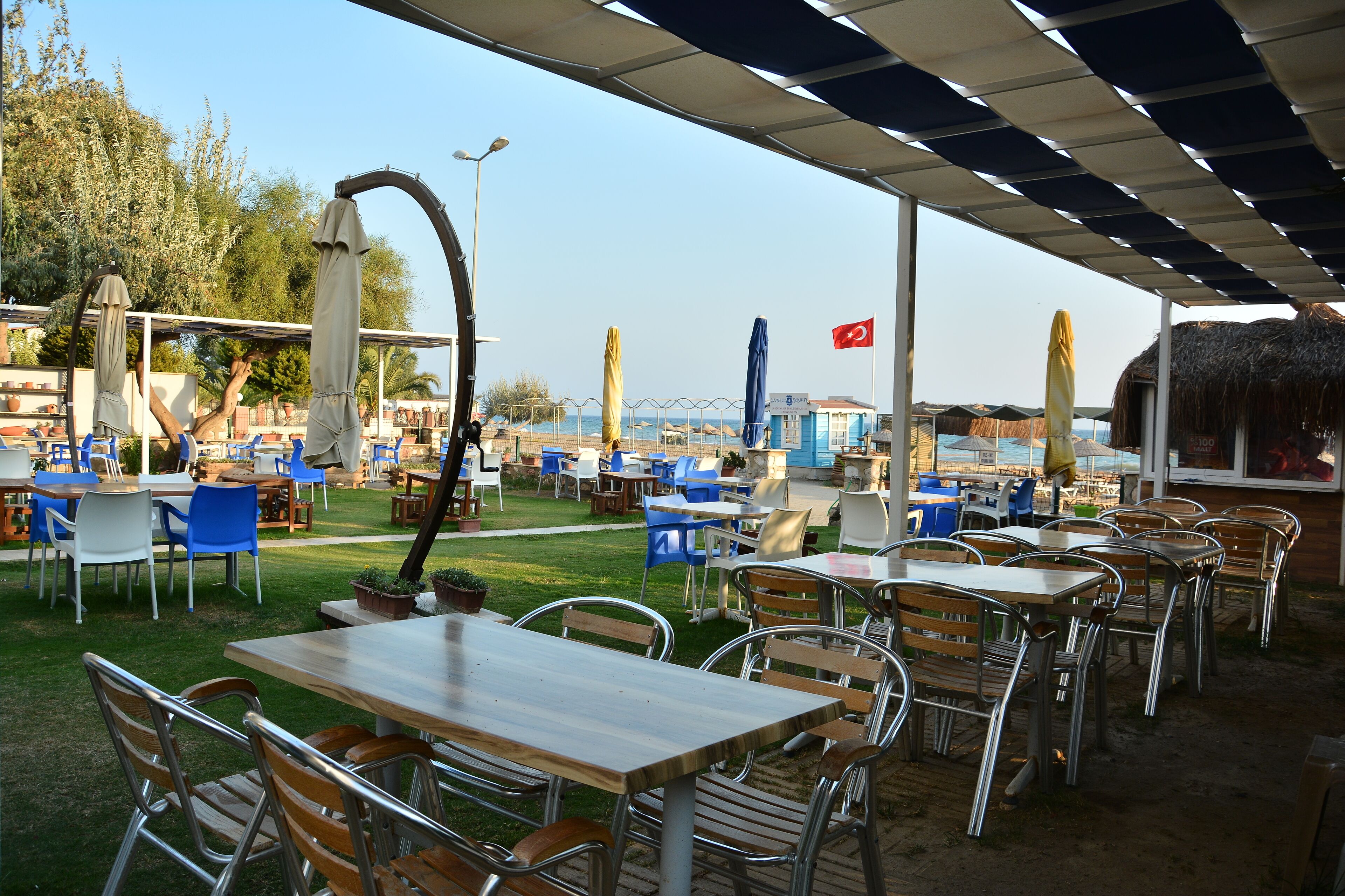 Un área de comedor al aire libre con mesas, sillas, sombrillas y vista al mar.