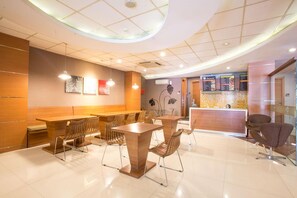 Een modern restaurant met een centrale eetruimte, een balie met een menukaart en een muur met abstracte kunst.