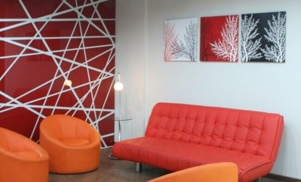 A modern room with a red sofa, two orange chairs, and abstract wall art.