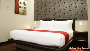 A Deluxe King Room with a large bed, a modern wall with a circular pattern, and a painting on the wall. - Citihub Hotel @ Tunjungan (Surabaya)