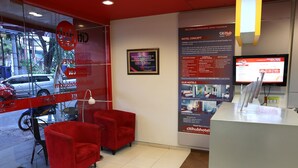 A hotel reception area with a glass wall, red chairs, and a digital screen displaying hotel information. - Citihub Hotel @ Tunjungan (Surabaya)