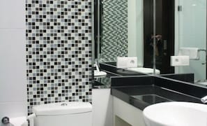 A modern bathroom with a black and white tiled wall, a white sink, and a large mirror. - Citihub Hotel @ Tunjungan (Surabaya)