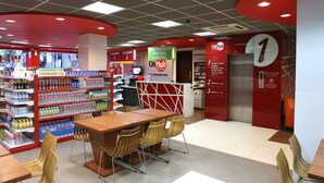 A hotel lobby with a red and white color scheme, a reception desk, a seating area with chairs, and a self-service kiosk. - Citihub Hotel @ Tunjungan (Surabaya)