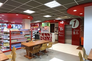 A hotel lobby with a red and white color scheme, a reception desk, a seating area with chairs, and a self-service kiosk.