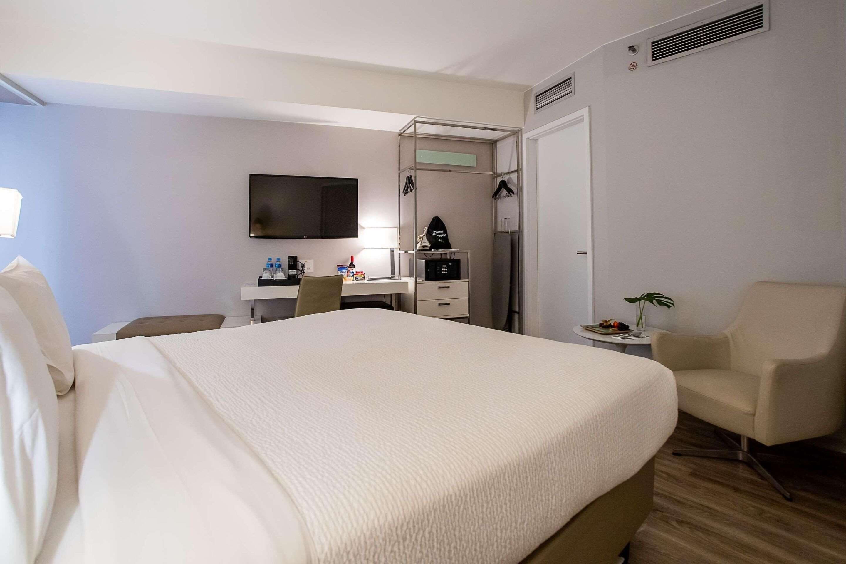 A hotel room with a large bed, a desk with a computer, a chair, and a television on the wall.