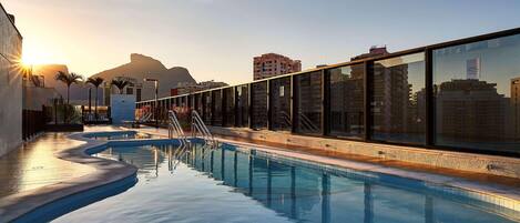 Una piscina al aire libre, sombrillas, sillones reclinables de piscina