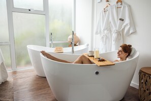 Un baño moderno con una bañera independiente, una bandeja de madera con una vela y un ventanal grande.