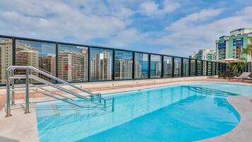 Una piscina al aire libre, sombrillas, sillones reclinables de piscina