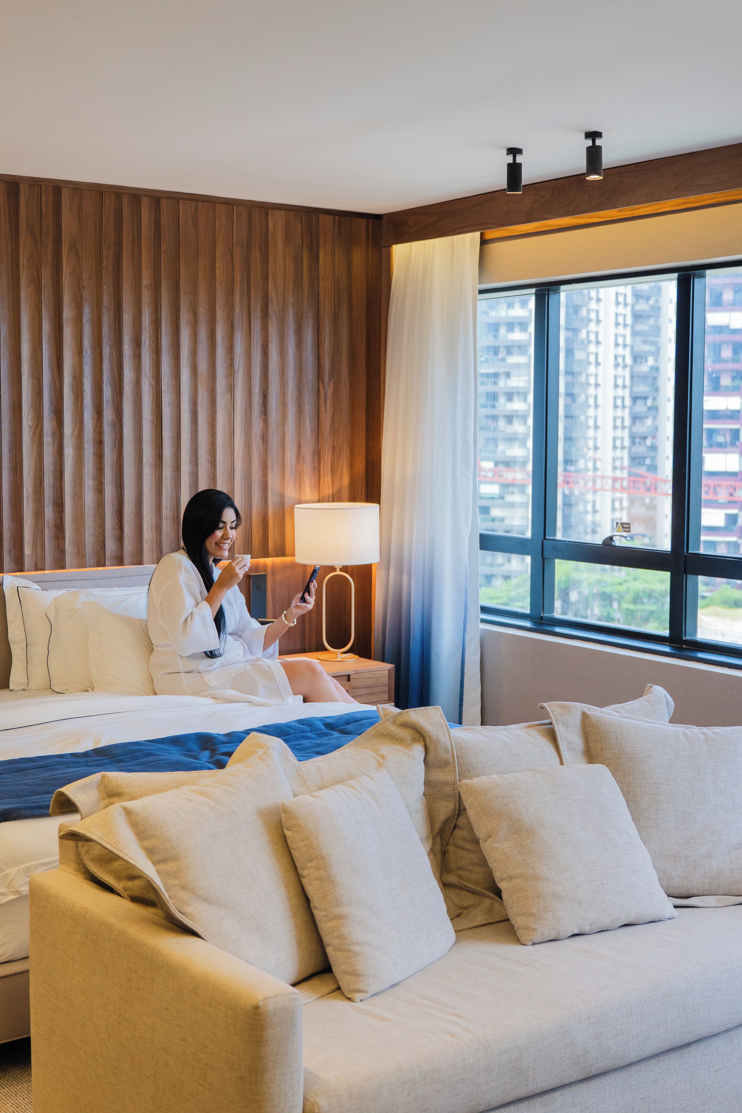Habitación de hotel con una cama, un sofá, una lámpara y una ventana con vistas a edificios.