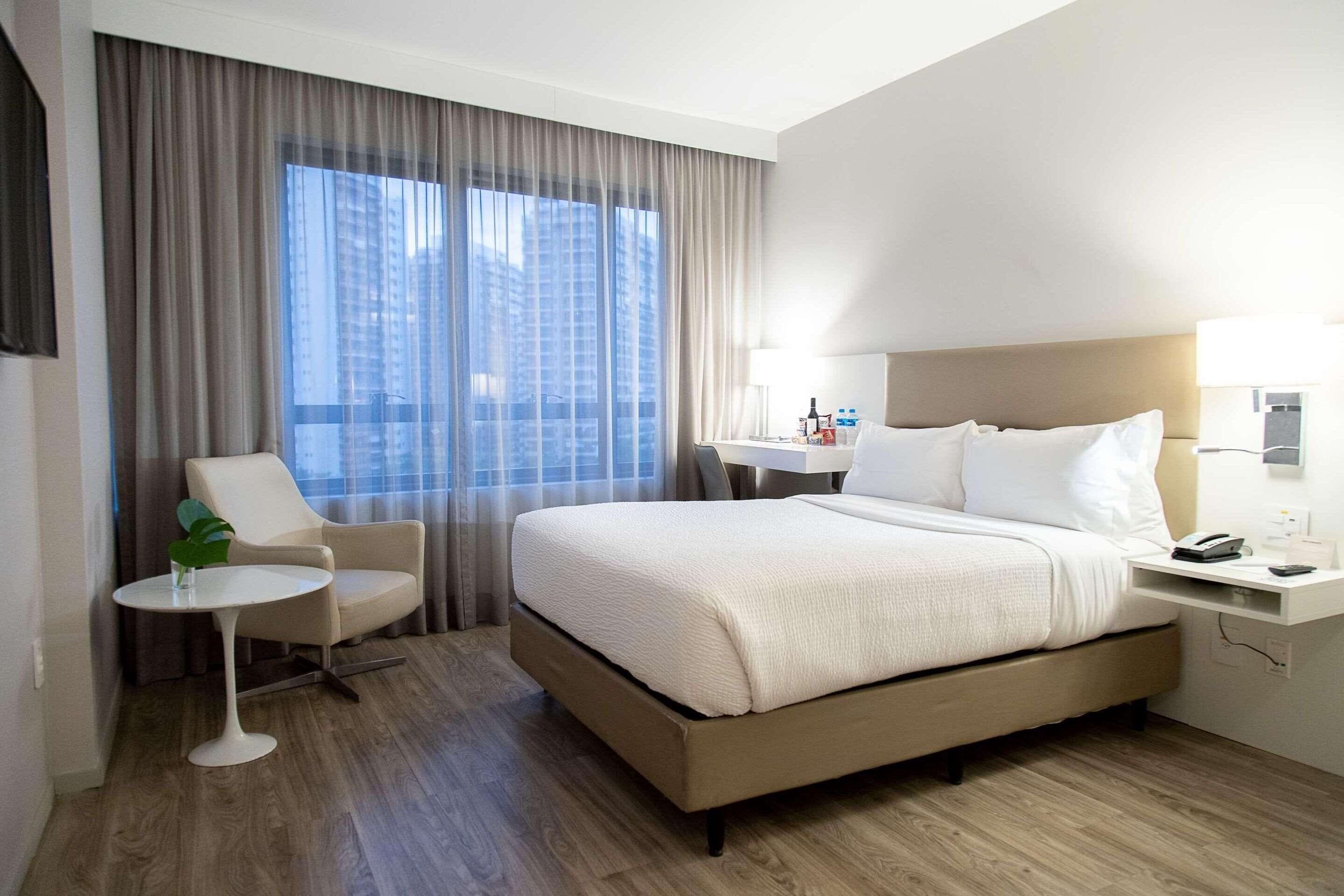 Habitación de hotel con una cama grande, una silla, una mesita pequeña y un escritorio con lámpara.