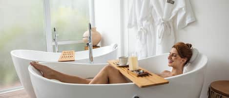 A person relaxing in a bathtub with a candle, a cup, and a tray with stones.
