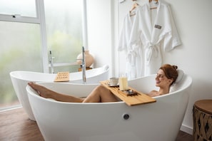 Una persona relajándose en una bañera con una vela, una taza y una bandeja con piedras.