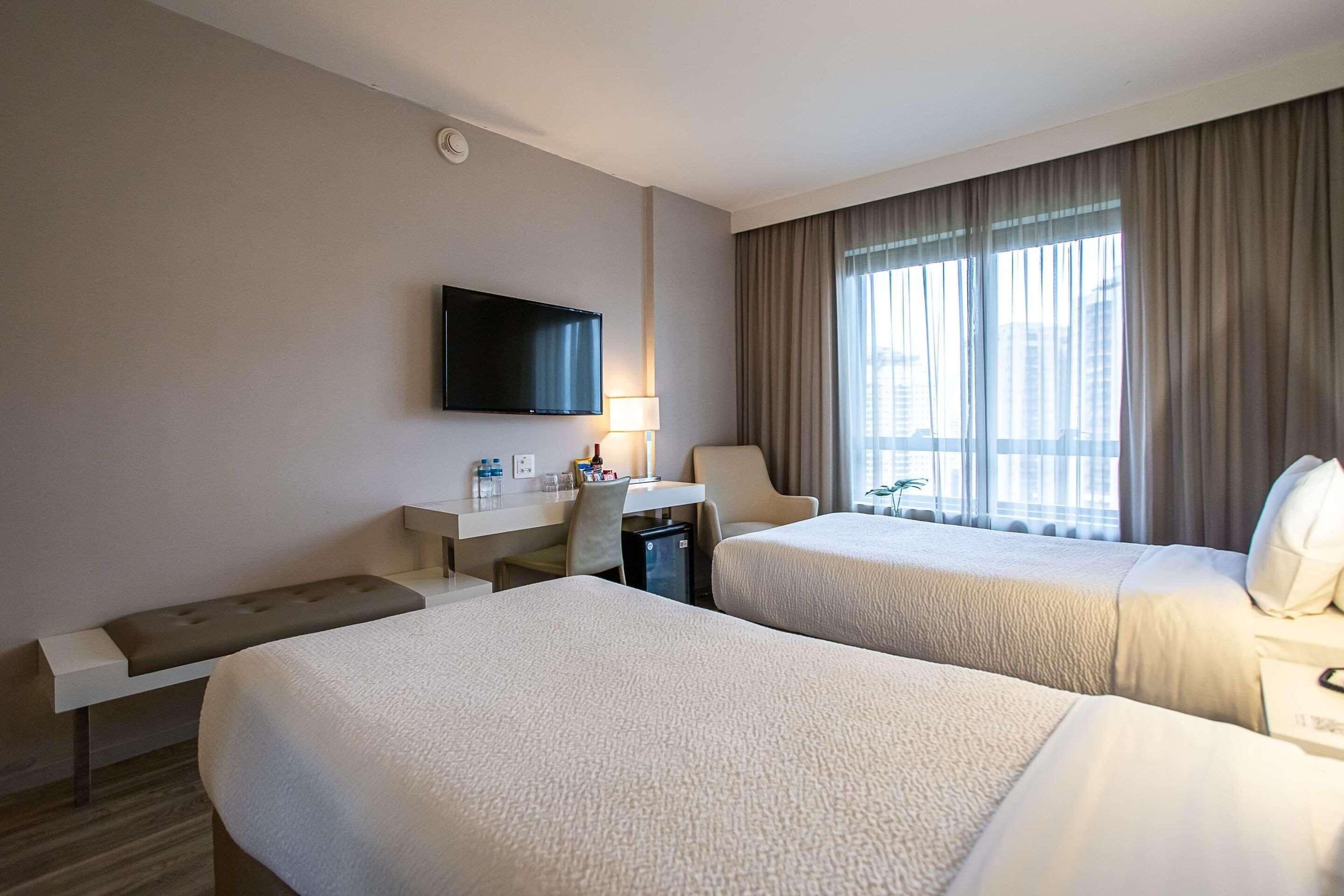 Une chambre d’hôtel avec deux lits, un bureau, une télévision et une fenêtre avec des rideaux.
