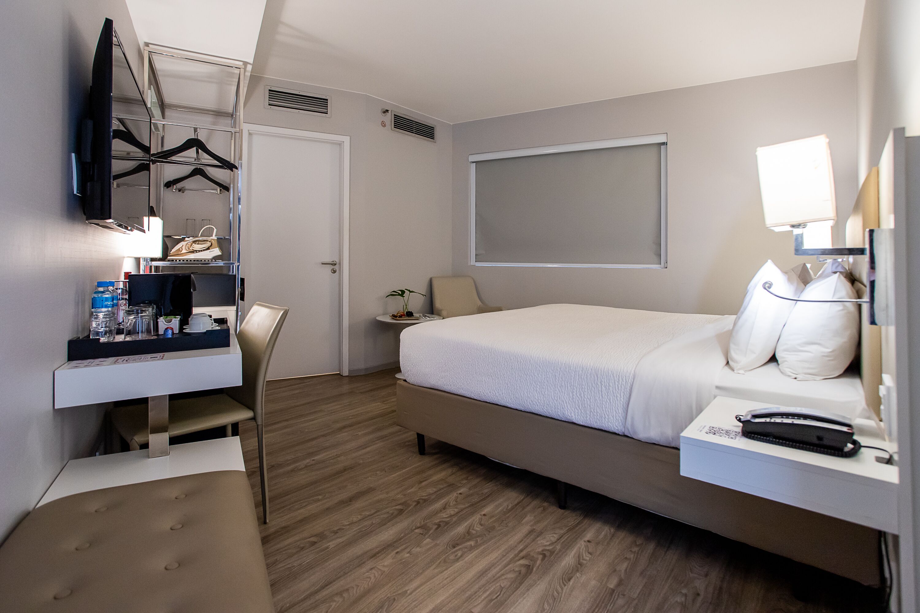 Ein Hotelzimmer mit Bett, Nachttisch, Lampe und einem an der Wand befestigten Fernseher.