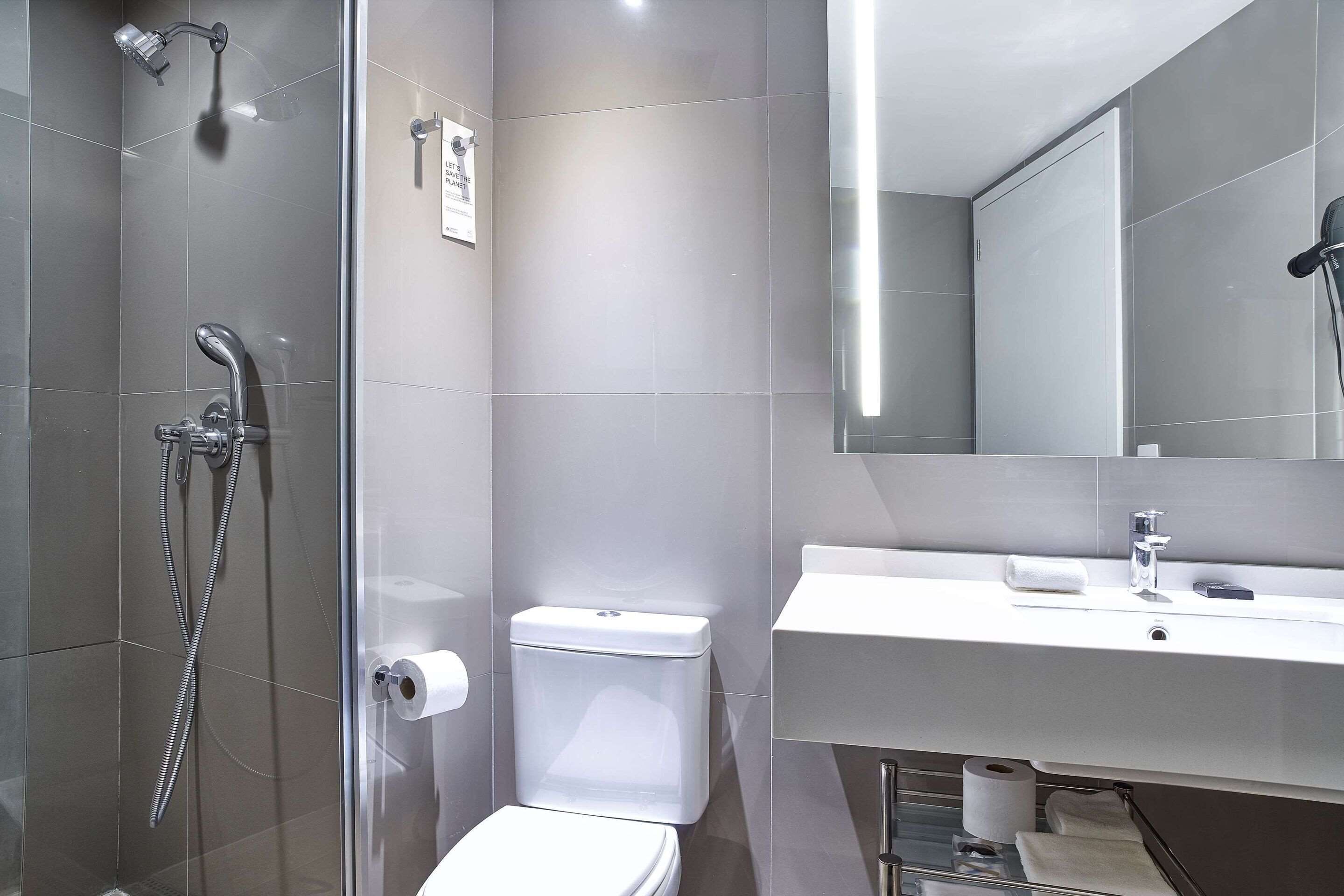 A modern bathroom with a glass shower enclosure, a white toilet, and a sink with a mirror above it.