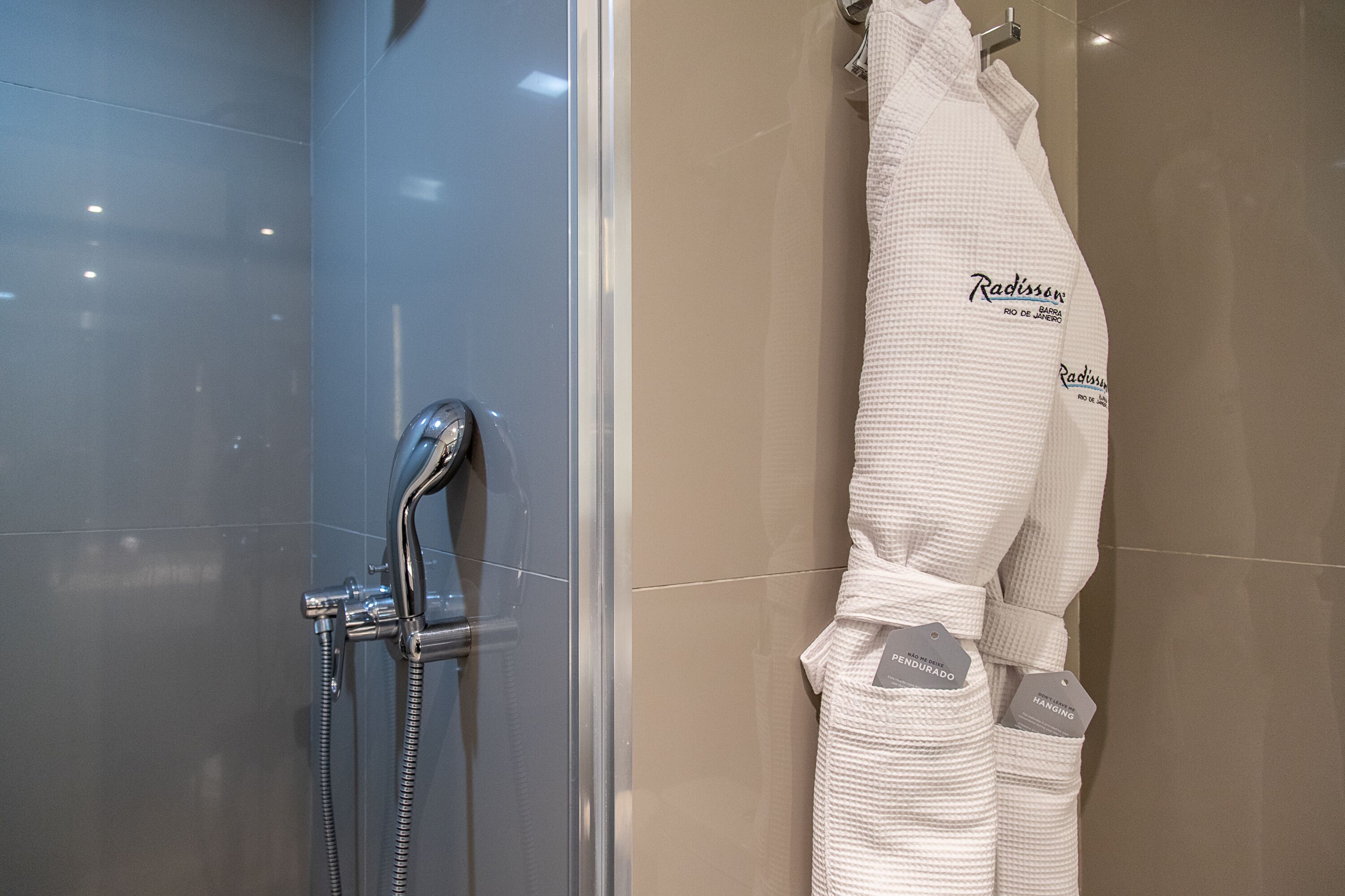 A bathroom with a glass shower enclosure, a towel rack with a white towel, and a bathrobe hanging on the wall.